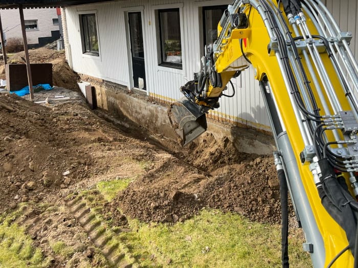 Grävmaskin schaktar längs en husgrund inför husdränering