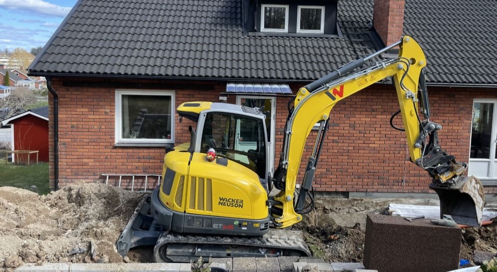 Grävmaskin gräver vid ett tegelhus inför husdränering